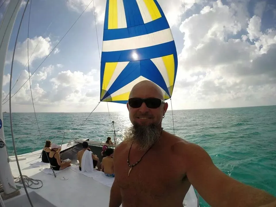Guests on a catamaran under a blue and yellow sail.
